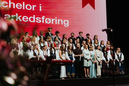 Kristianias avgangsstudenter står samlet på scenen under avgangsseremonien, iført bunader, kjoler og dresser.