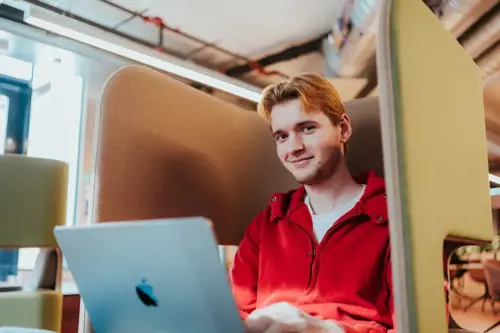En student med rød genser sitter med en Mac på fanget