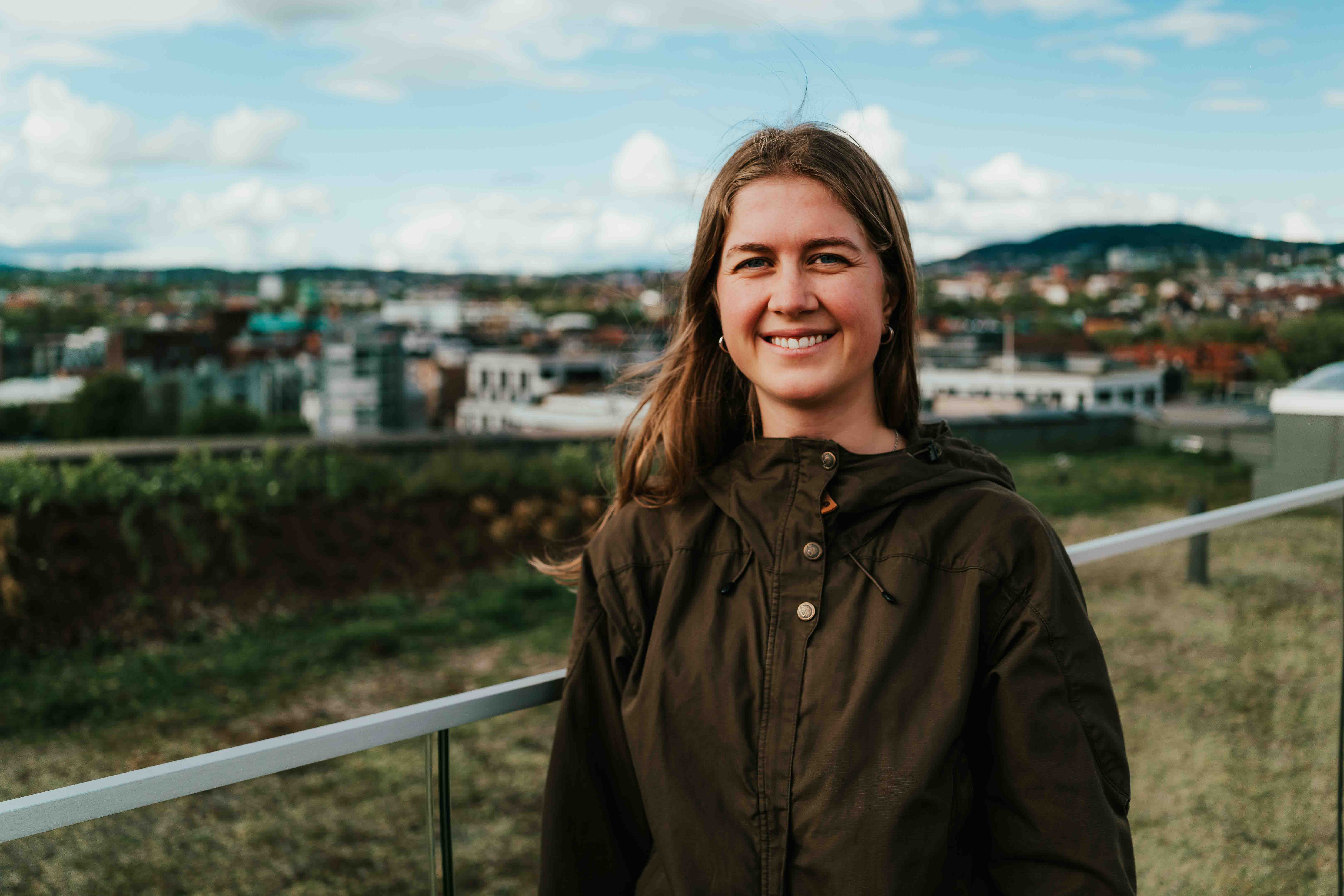 Mørkblond ung kvinne i mørkegrønn jakke på frodig takterrasse