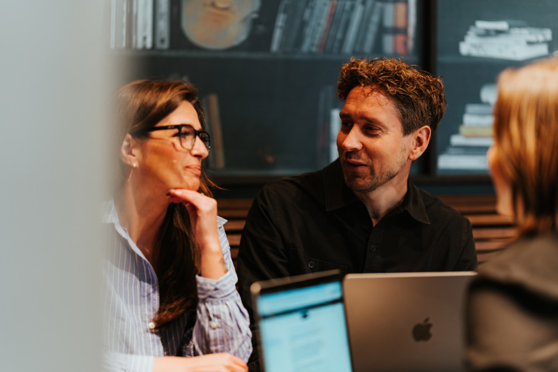 Tre mennesker sitter med PC-er ved et bord.