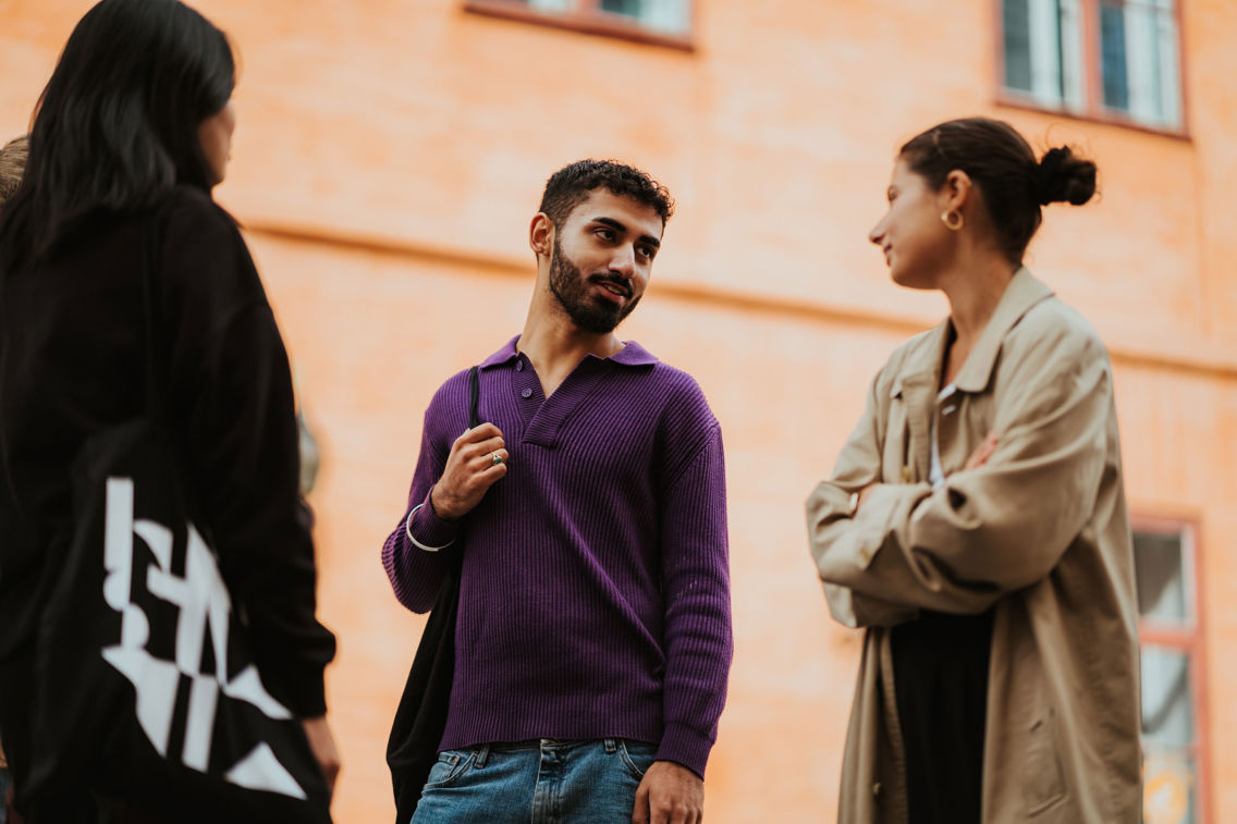 Tre studenter står i en gate, ved en murfasade.