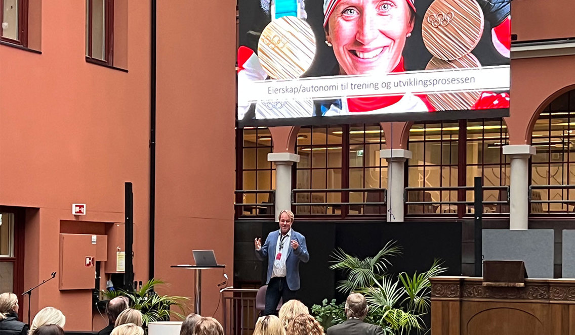 Professor Espen Tønnessen på podium med bilde av Marit Bjørgen  på storskjerm