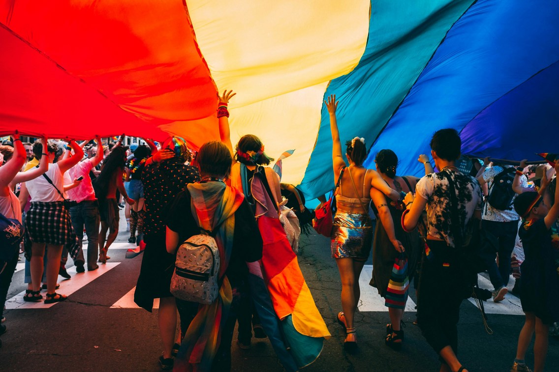 Mennesker i pride-paraden som går med et stort pride-flagg over seg