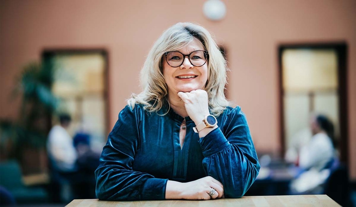 Påtroppende rektor Trine J. Meza smiler mot kamera mens hun hviler haken på hånda. Hun har på seg en mørk blå velour kjole og sorte briller