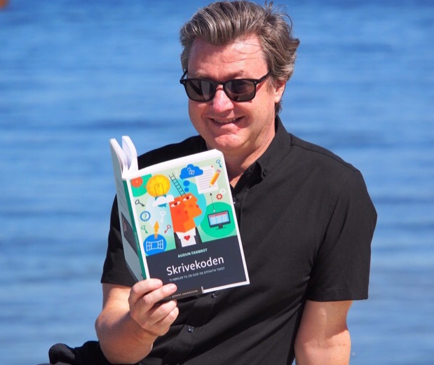 Mann med solbriller leser bok med havet i bakgrunnen.