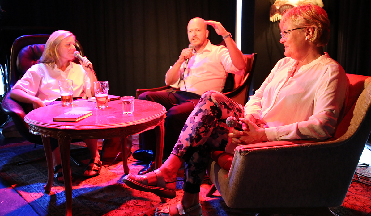 Bilde fra boklansering av "Jakta på makta - 12 råd for effektiv påvirkning". Avbildet er Trine Eilertsen, Sigbjørn Aanes og Kristin Halvorsen. De sitter på en scene i retro stoler med et rødt scenelys som dekker dem.