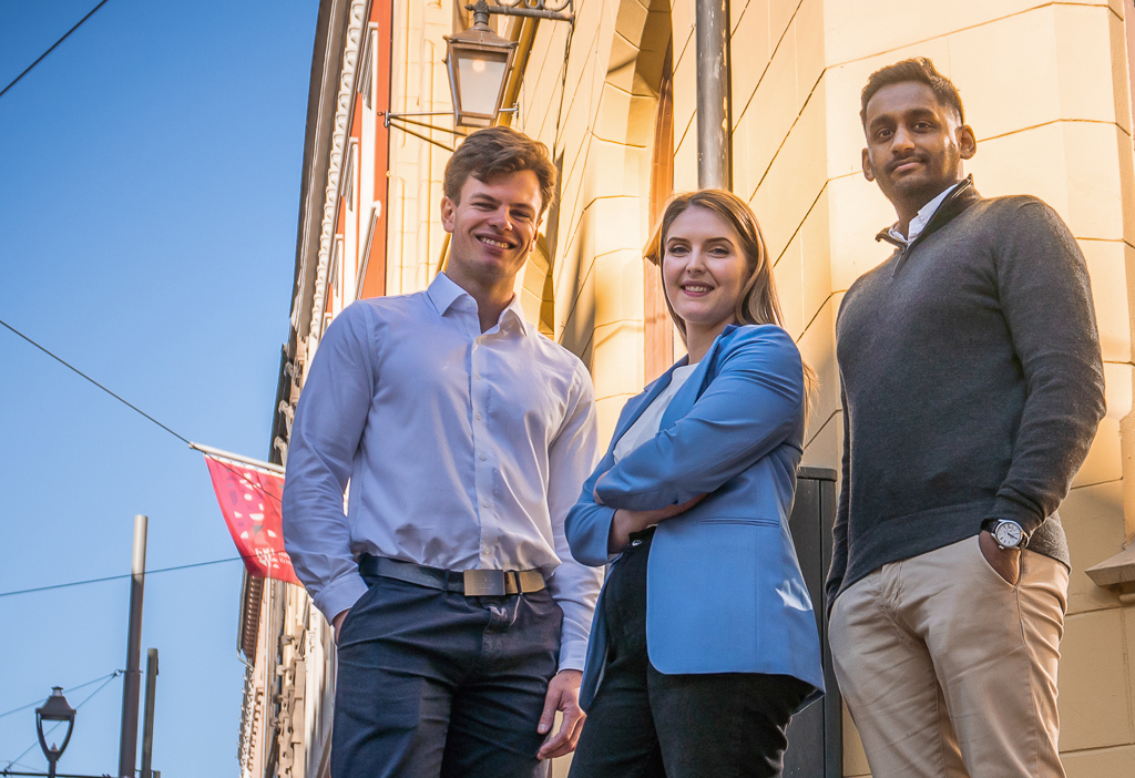 Tre studenter foran en murfasade.