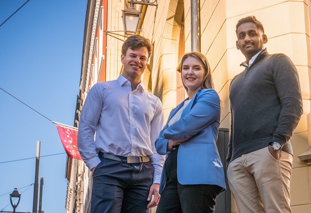 Tre studenter foran en murfasade.