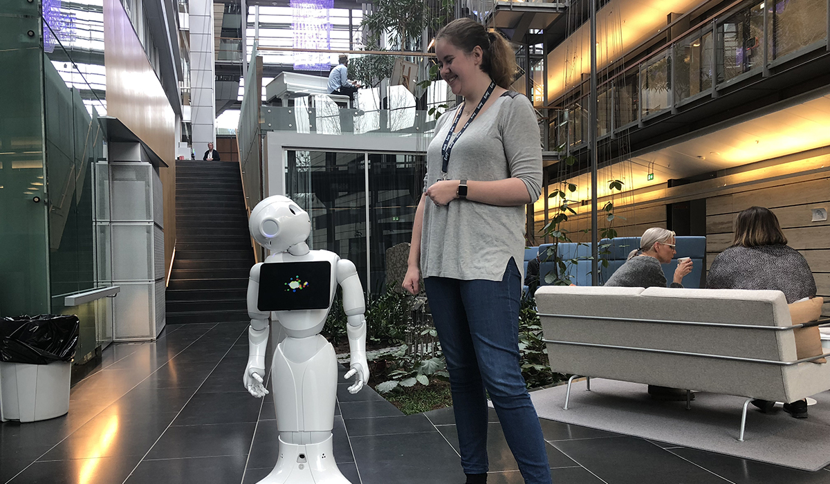 Jente og robot ser på hverandre i et kontorlandskap.