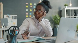 En kvinne som hviler hodet på armen som sitter foran pc-en og stirrer tomt ut i luften