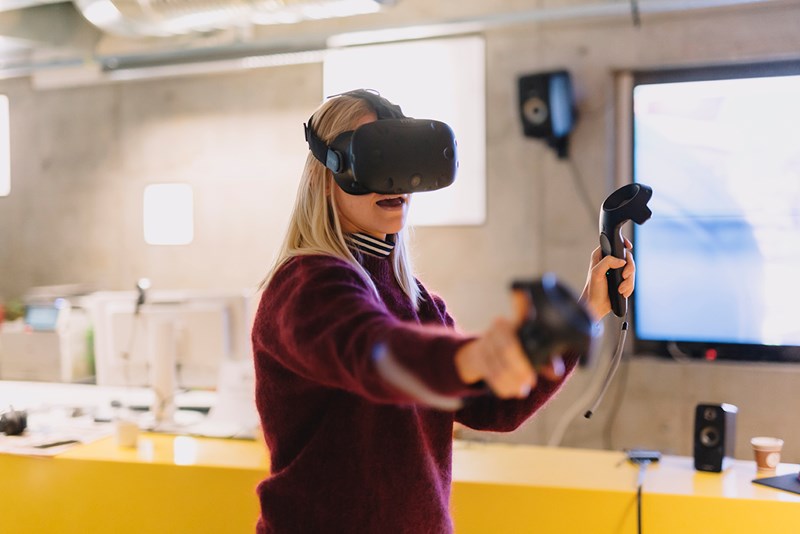 Foto av en jente som står å spiller med VR-briller og håndtak i klasserommet.