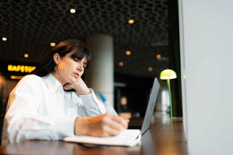 En person i en hvit skjorte er dypt konsentrert om sitt arbeid på en bærbar datamaskin i et moderne offentlig rom.
