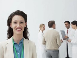 Female doctor smiling into the camera with a group of doctors talking behind her.