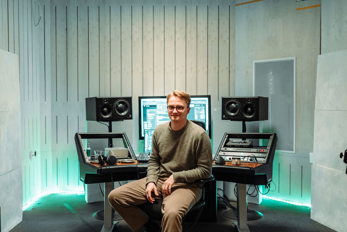 Herman sitter på en stol foran arbeidspulten, PC-skjerm og store høyttalere.