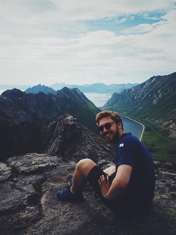 Foto av mann som sitter på fjell og smiler til fotograf