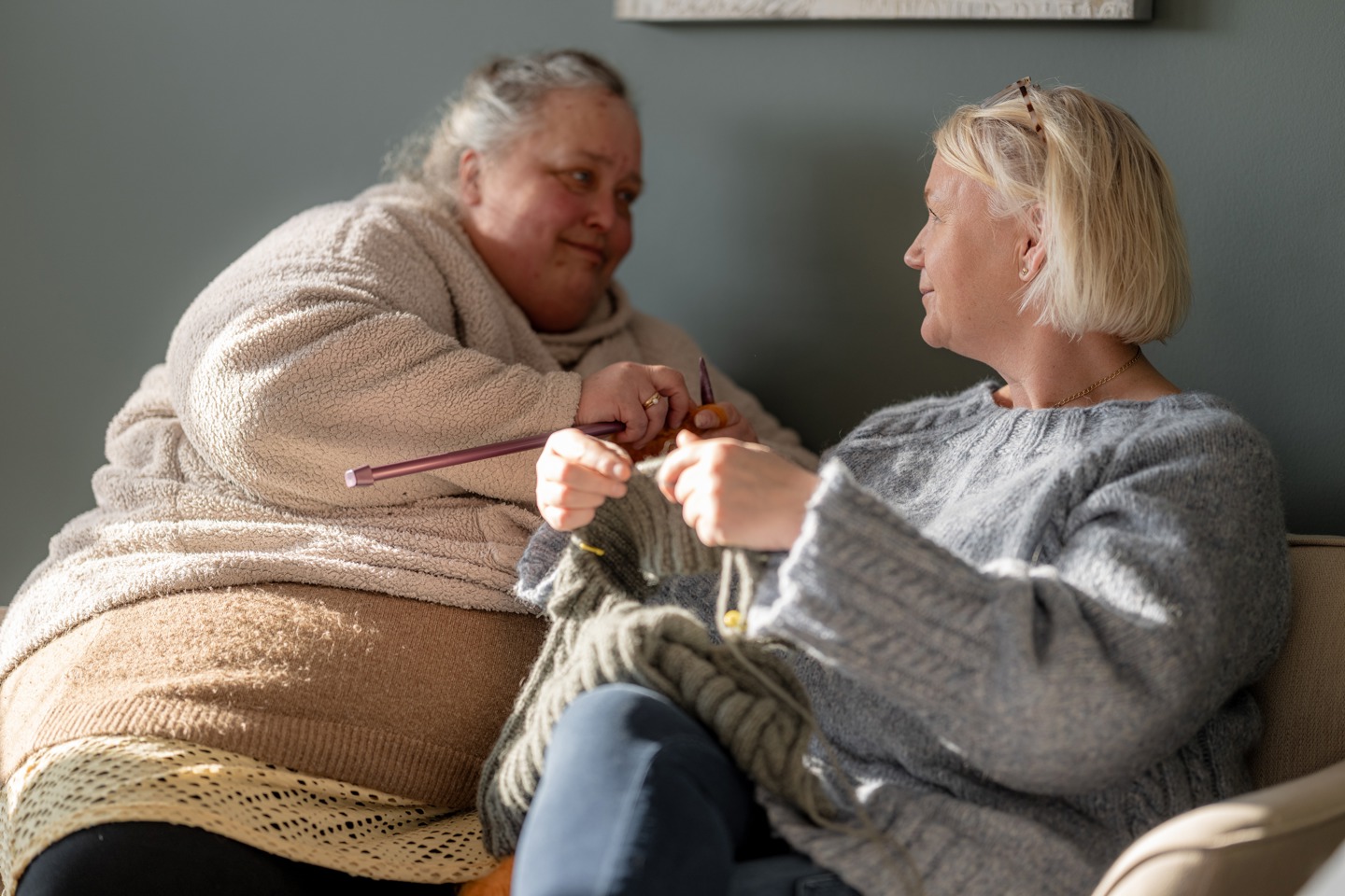 To personer sitter i en sofa og strikker sammen i et rom med mykt dagslys