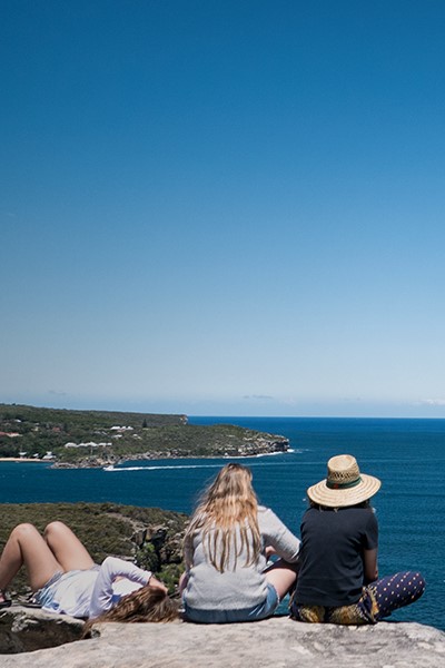 Tre jenter sitter på et utsiktspunkt og ser utover havet.