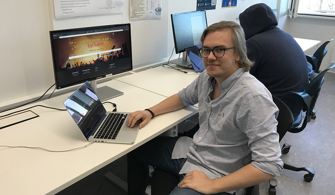Bildet viser en student som sitter på en stol mens han har den ene armen på beinet og den andre armen på pcen. Han har briller og har på seg lyseblå skjorte. 