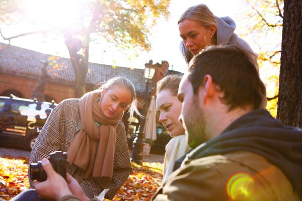 Foto av tre studenter i en park som ser på et kamera.