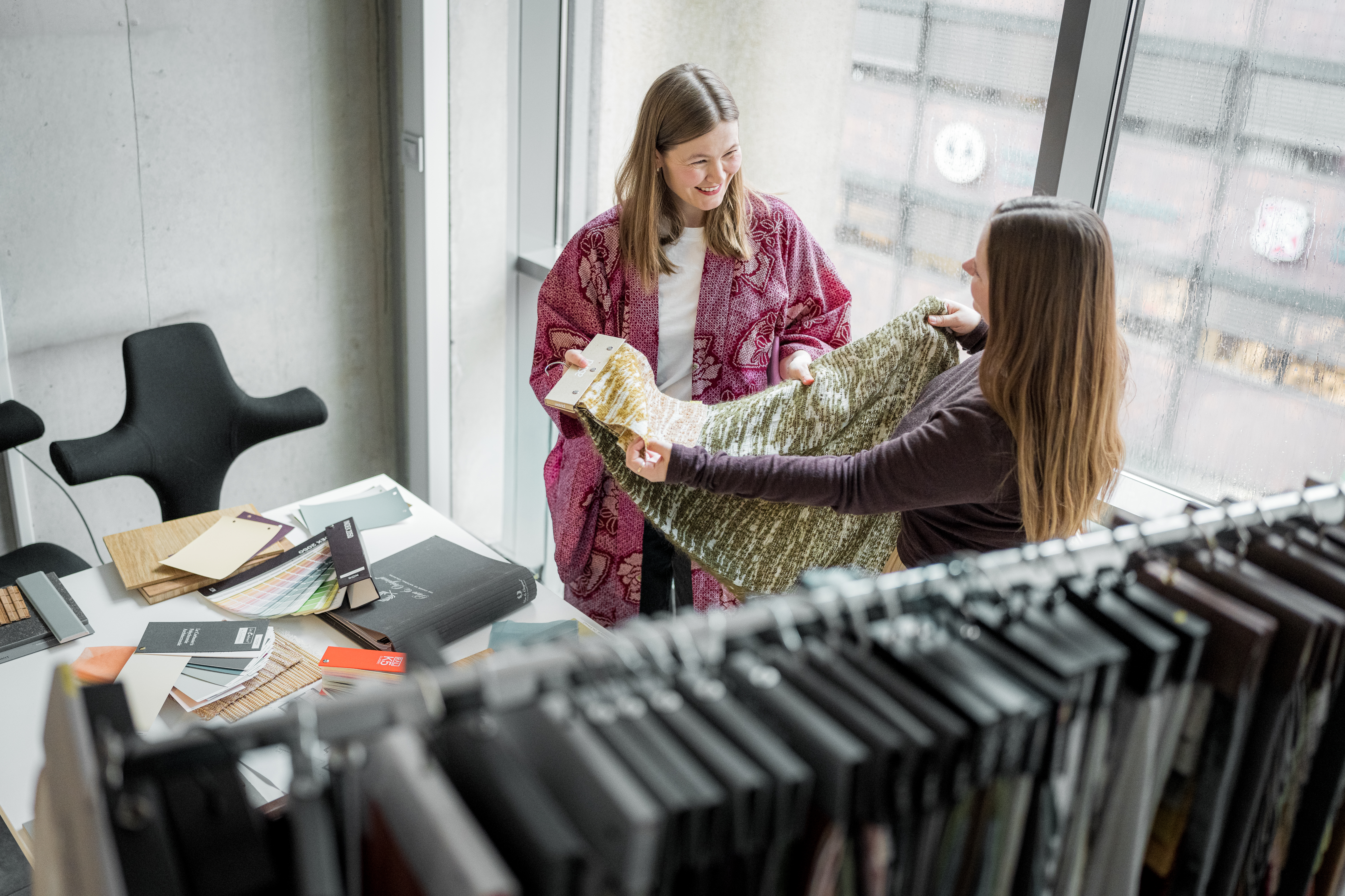 To personer står ved et bord og ser på tekstilprøver og materialer i et interiørprosjekt