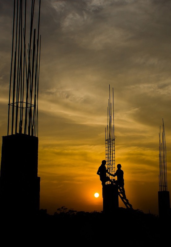 Foto av byggeplass i solnedgang, med to silhuetter av arbeidere.