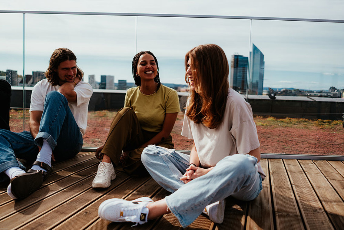 Foto av tre studenter som sitter på en promenade