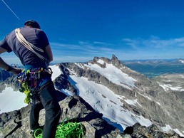 Mann med klaetreutstyr på en fjelltopp i solen