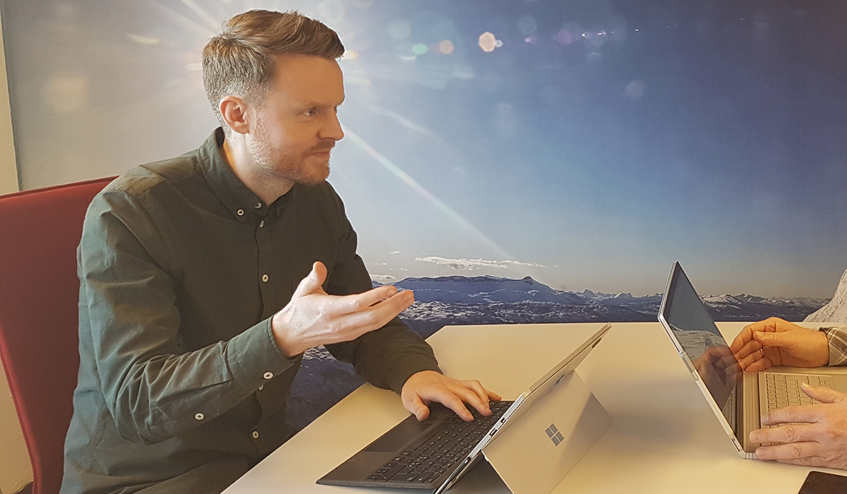 salgsledelse - Andreas Fjørtoft sitter med en datamaskin foran seg og forklarer noe til en annen person.