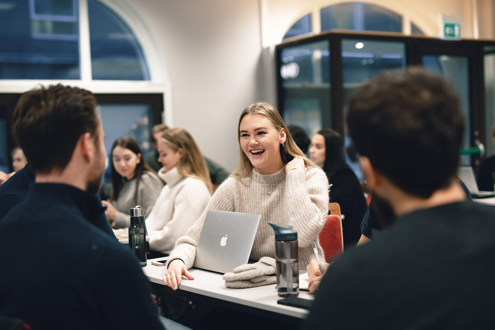 Studenter diskuterer rundt et bord. Bachelor i ledelse og servicestrategi ved Høyskolen Kristiania.