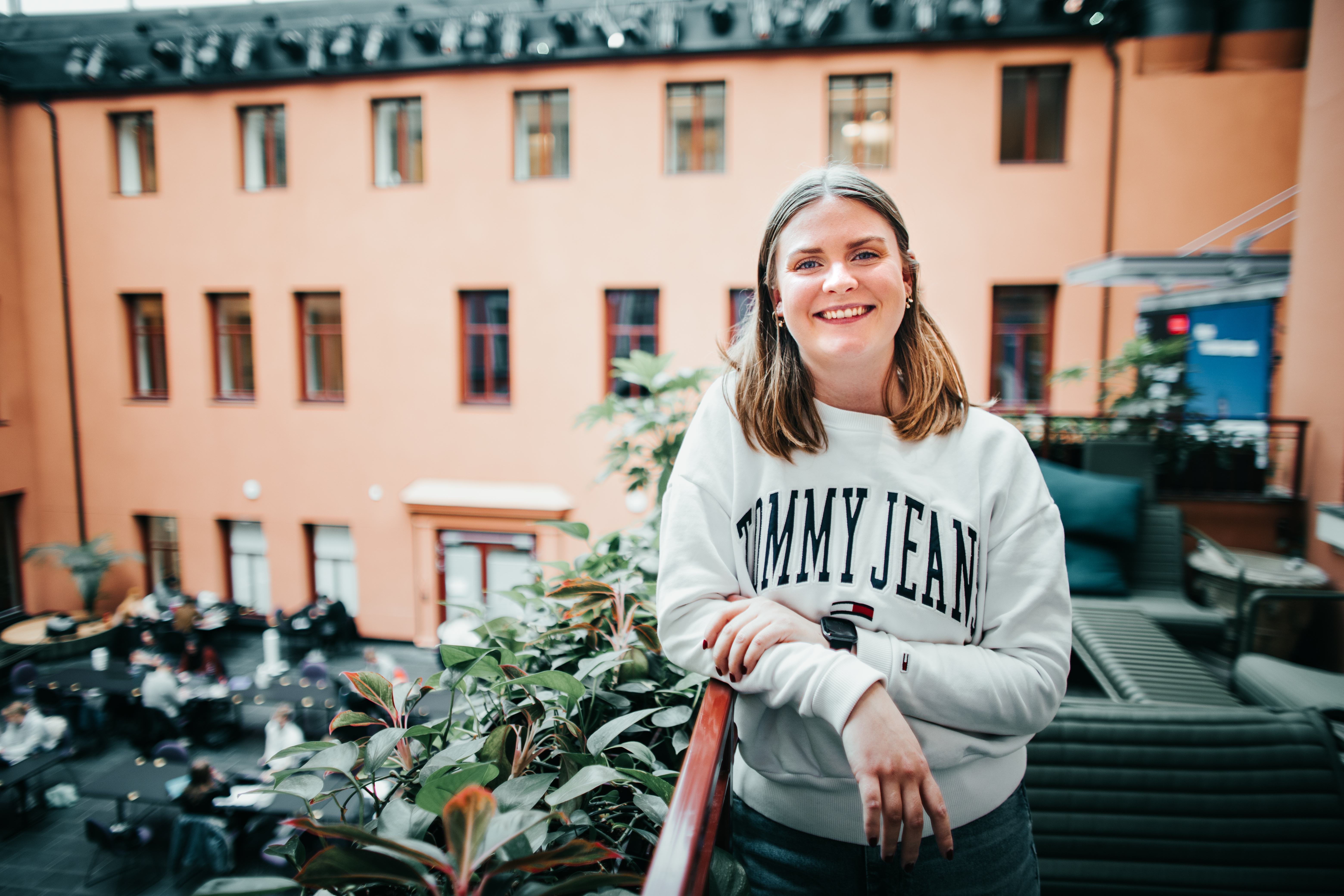 Masterstudent Maren Lindseth i Høyskolen Kristiania sine lokaler i kvadraturen, Oslo. Iført hvit genser lener hun seg på et rekkverk med grønne planter.