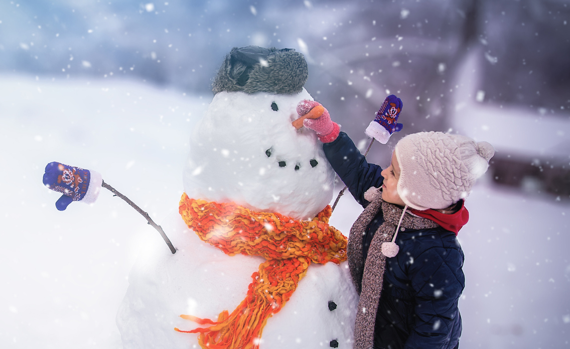 Lliten jente fester gulrotnese på snømann mens det snør lett