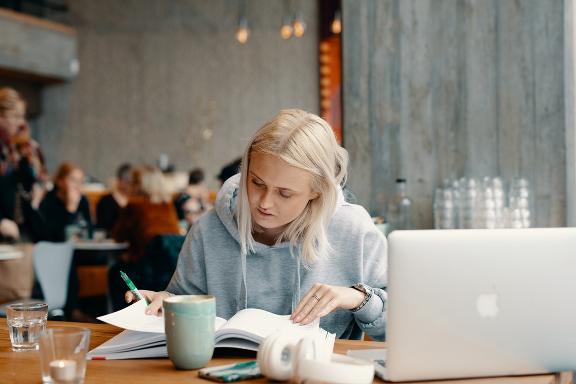 Foto av kvinnelig student på kafé som leser i en bo.