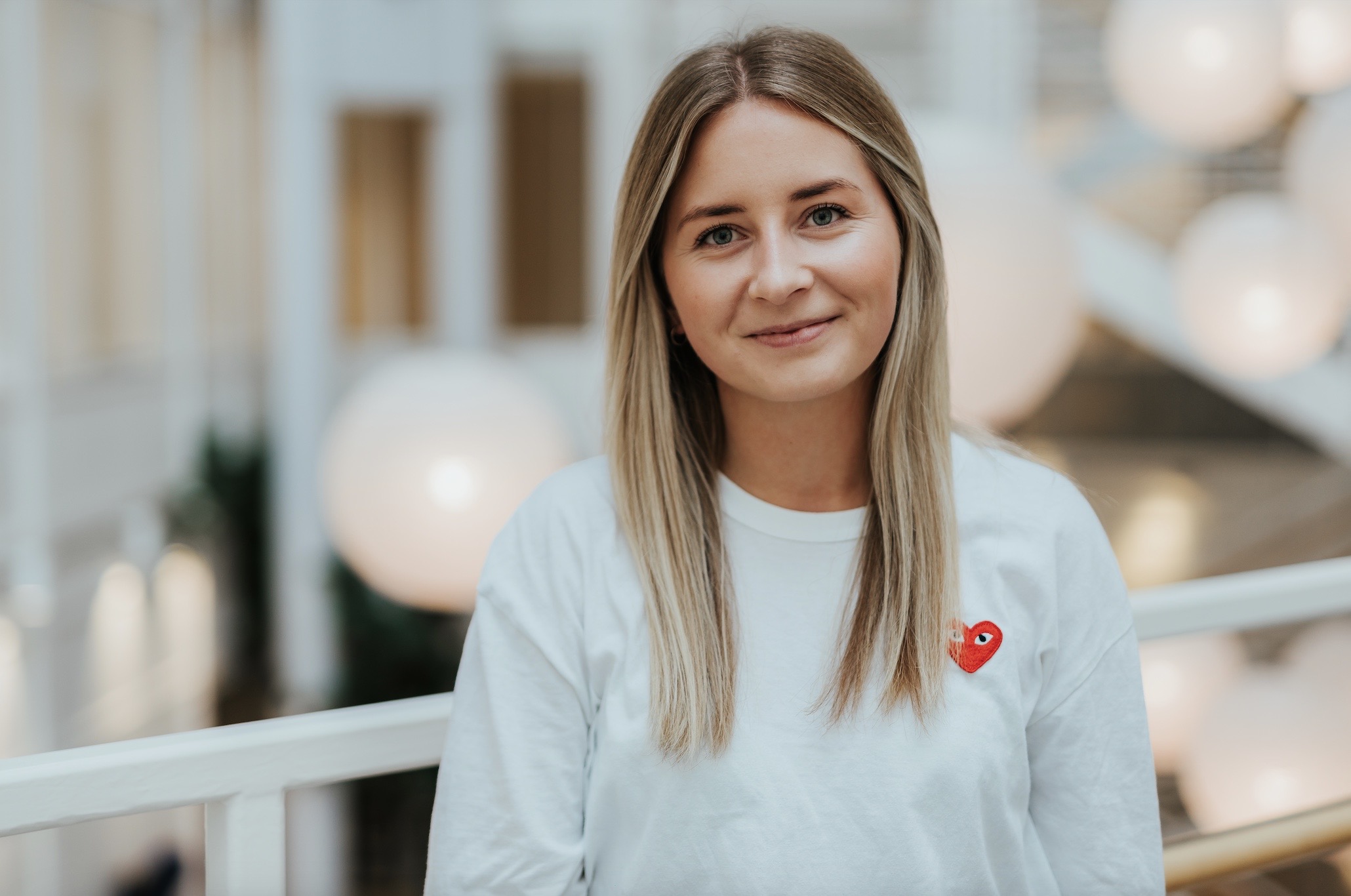 Mathilde Hogsnes smiler mot kamera. Hun står innendørs, ser avslappet ut og har på seg en hvit genser. Foto.