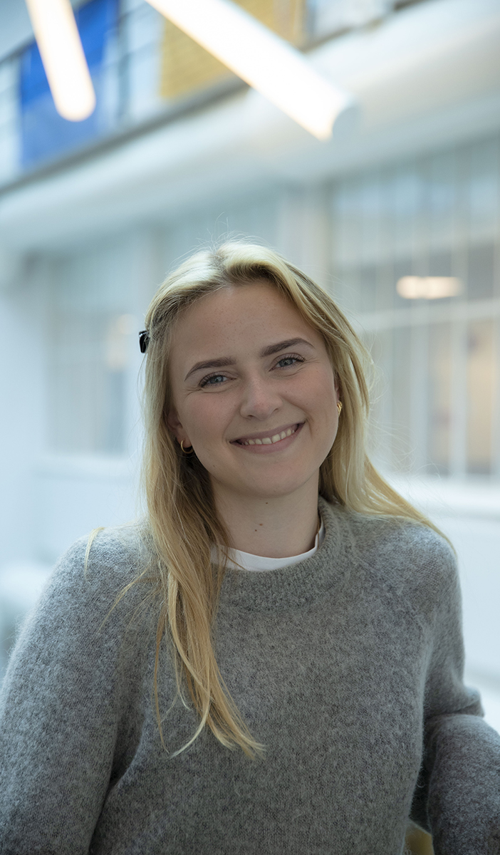 Kristiane Lunde studerer Music Business ved Fagskolen Kristiania. Hun lener seg på gelenderet i trappen på Campus Fjerdingen med foajeen i bakgrunnen. Kristiane har langt, blondt hår, mørke øyenbryn og blå øyne. Hun har på seg en sort hårspenne, gulløredobber og en hvit topp med en grå ullgenser over.