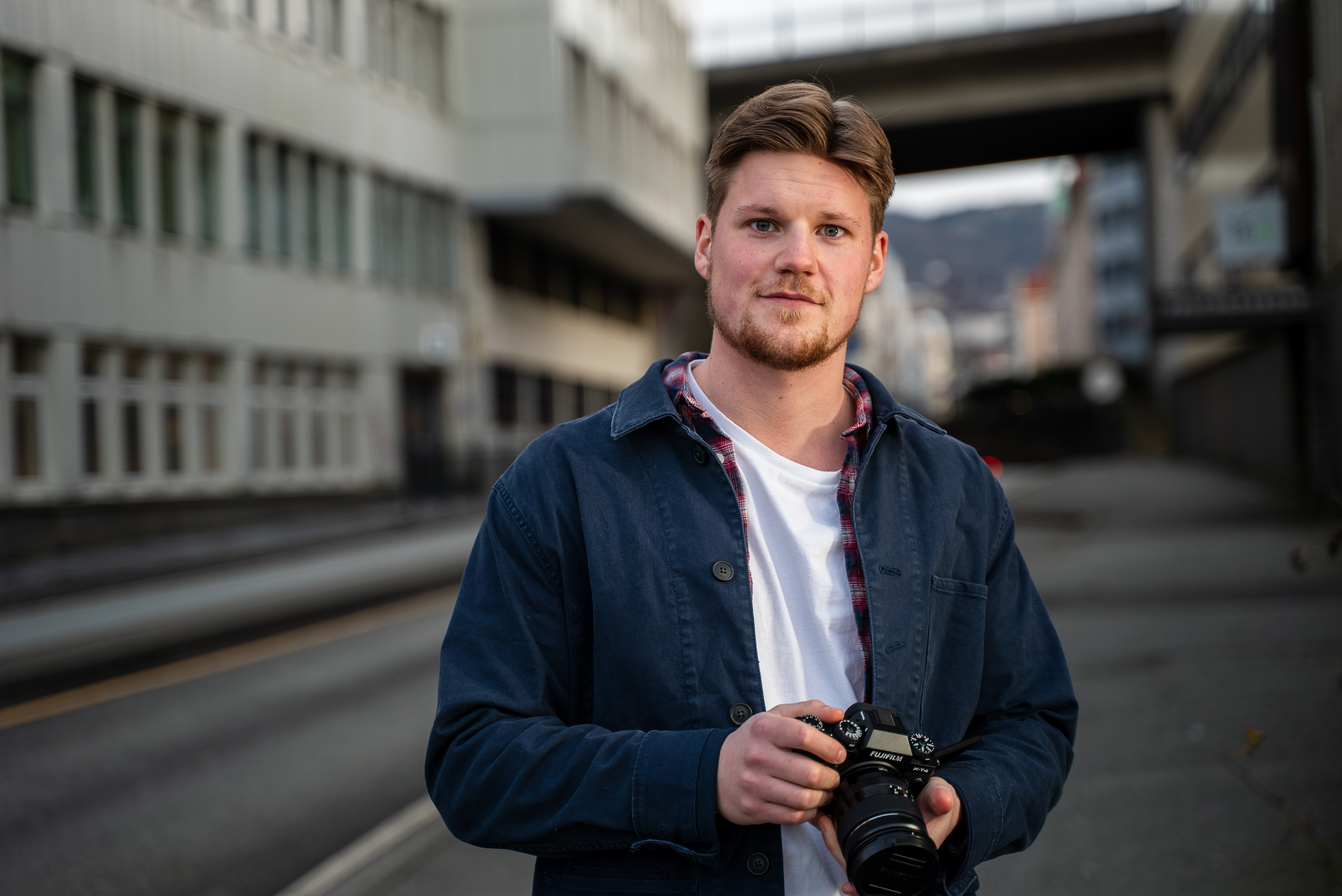 Oliver står ute på gangfeltet utenfor kontorlokalene til Amesto. Han har et kamera i hånden og ser i kamera. 