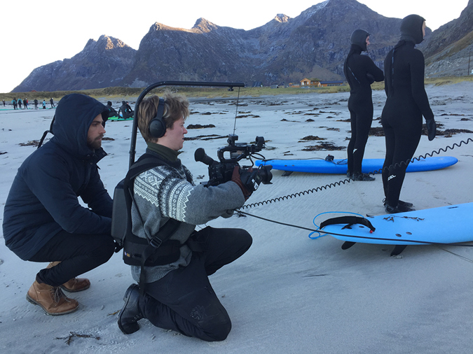 Fire studenter på en strand med surfebrett filmer en scene.