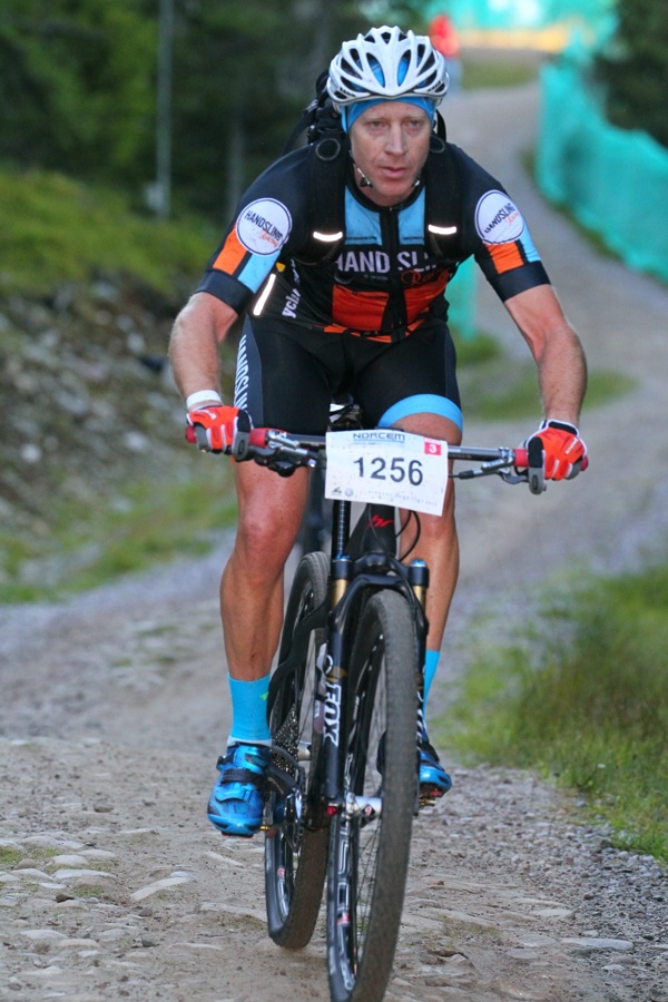Nigel Halpern is cykling in a race, with a helmet, professional clothes and with his participant number in front on his bike.