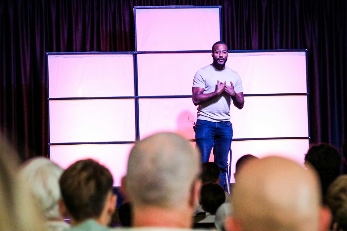 En ung mann står på scenen og prater foran publikum