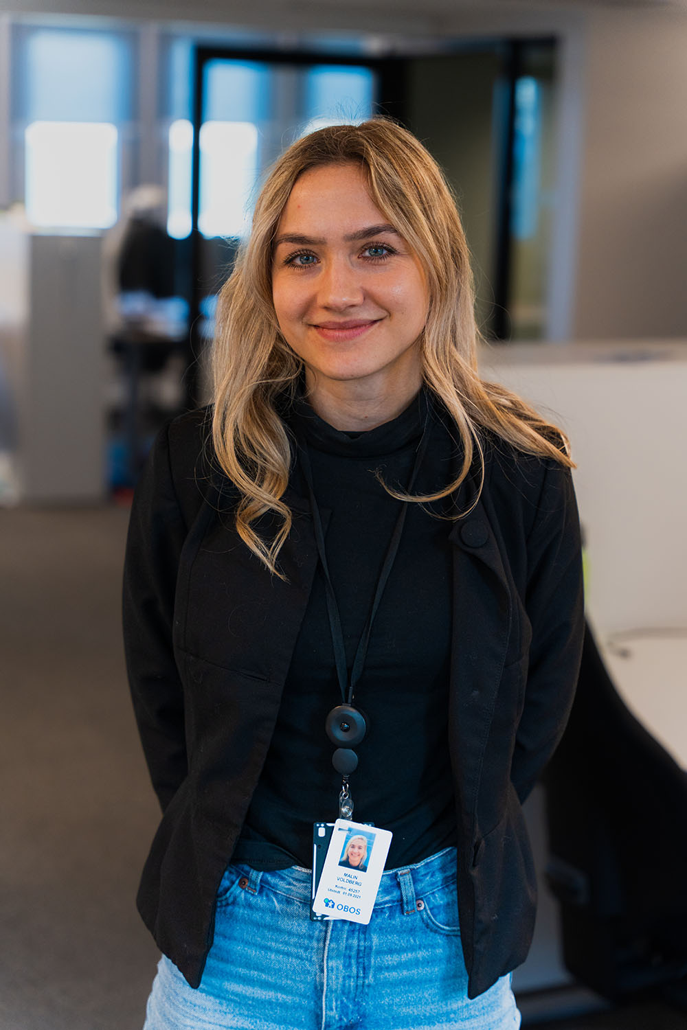 Portrett av Malin Voldberg som står i et kontorlandskap og smiler til kamera