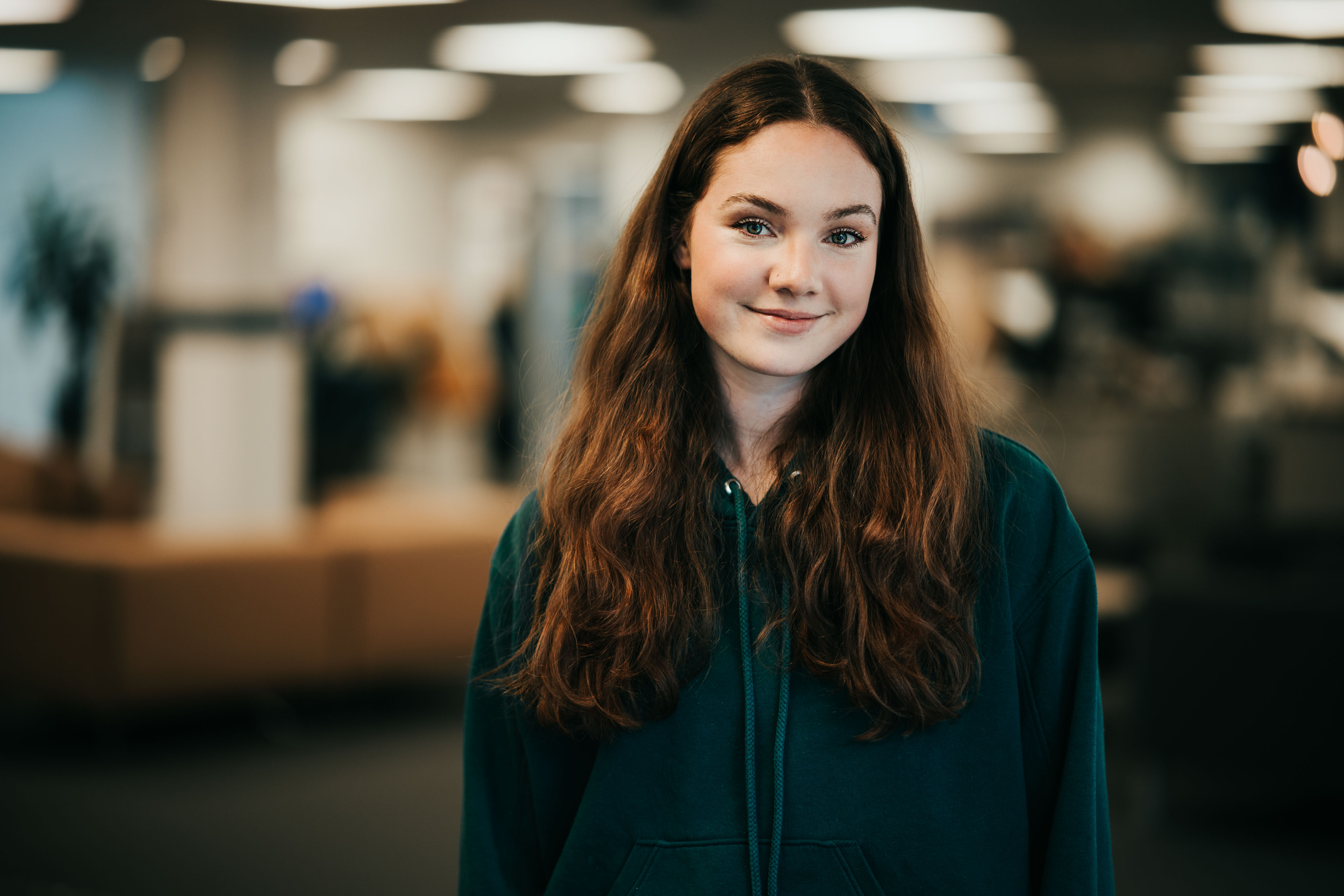Foto av ung kvinne i grønnblå hettegenser i et bibliotek.