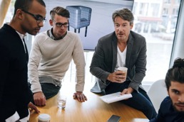 En gjeng står og snakker rundt et bord på jobb