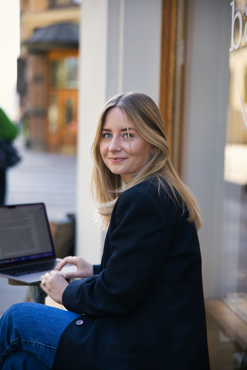 Mathilde Hogsnes sitter med en PC på kafeen Backstube og smiler inn i kamera