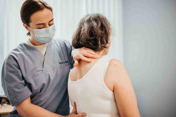 Kvinne med munnbind behandler en pasients rygg.