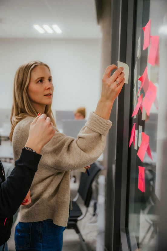 Studenter diskuterer idèer ved å henge post-it lapper på veggen. 