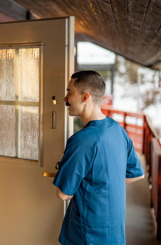 Helsefagarbeider i blå uniform åpner en ytterdør til en bolig