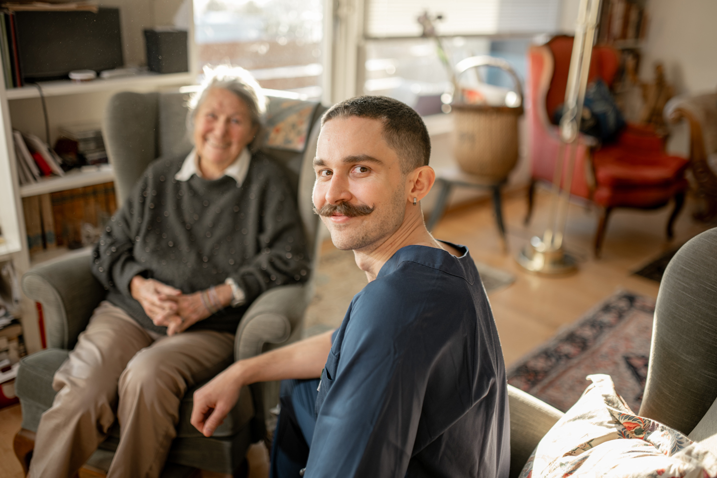 Helsefagarbeider og en eldre person sitter sammen i en stue