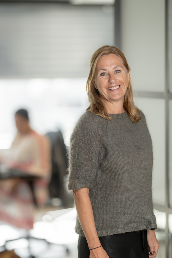 Fagansvarlig står i et kontormiljø og smiler til kamera