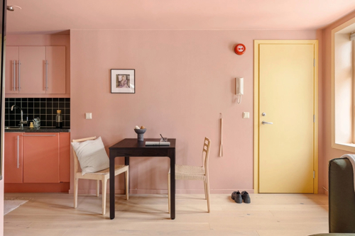 Spisestue innredet minimalistisk med rosa vegger og gul dør.