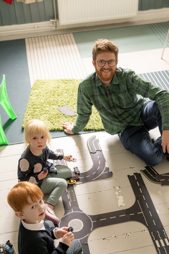 Barnehageansatt og to små barn sitter på gulvet og leker i en barnehage