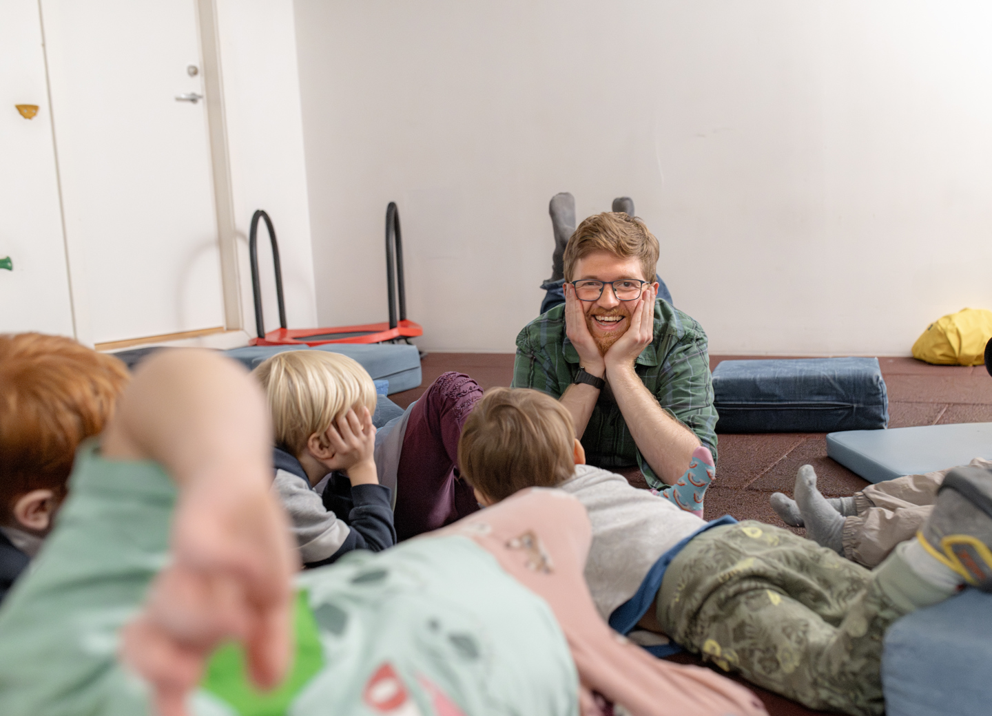 En gruppe barn ligger på matter og lytter til en voksen på et lekerom